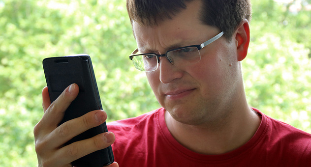 Ein junger Mann blickt skeptisch auf ein Smartphone, das er vor sich in der Hand hält. Foto: checked4you