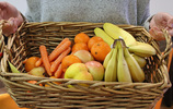 Eine Frau trägt einen Weidenkorb mit Möhren, Äpfeln, Clementinen und Bananen. Foto: checked4you.de