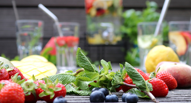Viele Früchte scharf im Vordergrund, Gläser und Karaffe mit Wasser und Fruchtstücken unscharf im Hintergrund. (Bild: Verbraucherzentrale NRW)