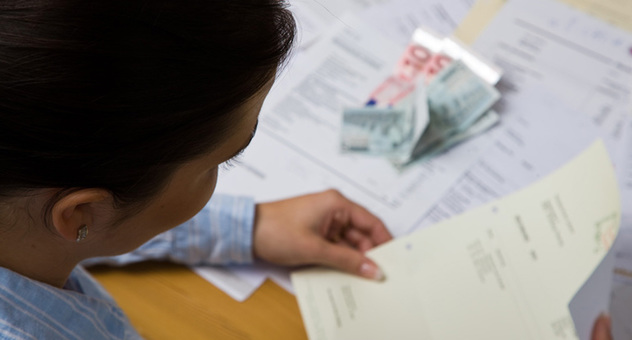 Frau mit Rechnung in der Hand, weitere und Geldscheine liegen vor ihr auf dem Tisch. (Foto: GinaSanders / Fotolia)