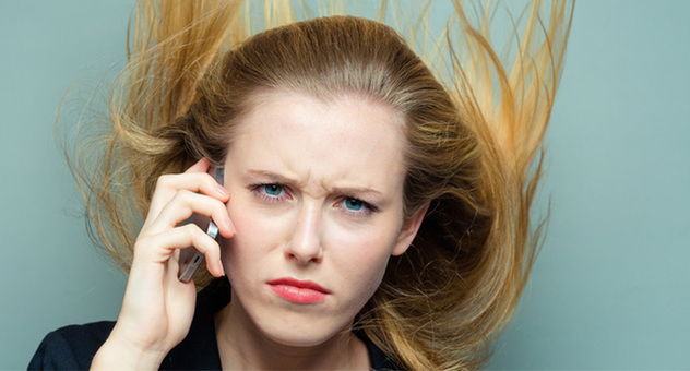Frau mit Smartphone am Ohr, grimmigem Blick und nach oben fliegenden blonden Haaren. Foto: conorcrowe/Fotolia.com