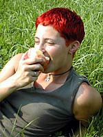 Oberkörper einer Frau, die im Gras liegt und in einen Apfel beißt